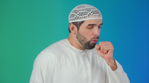 إيماءات الإرهاق والتعب الشديد، الإصابة بالأنفلونزا ونزلات البرد,الكحة والتهاب الحلق والحاجة للعلاج، بورتريه لرجل عربي خليجي اماراتي يرتدي الكندورة والطاقية يضع يده أمام فمه ويقوم بالسعال, خلفية ملونه