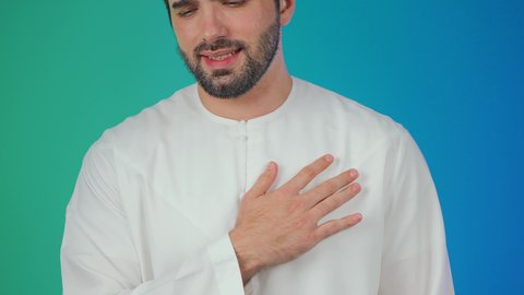 التعب والإرهاق والضغوطات النفسية, الشعور في زيادة معدل ضربات القلب, الاحساس بذبحه صدريه، بورتريه مقرب لرجل عربي خليجي اماراتي يرتدي الكندورة والقبعة البيضاء يضع يده على قلبه ويشعر بحالة سيئة من الوخز والألم, اضطرابات وأمراض قلبية, خلفية ملونة
