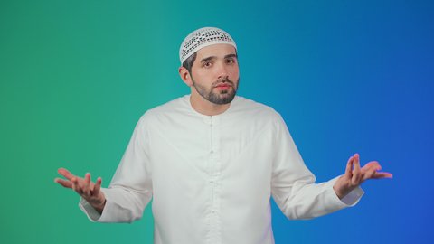 التساؤل والإستغراب والاستفسار عن أمر ما،  الغموض وعدم الوضوح، الإستفهام حول موضوع معين, بورتريه لرجل عربي خليجي اماراتي يرتدي الكندورة والقبعة البيضاء يرفع يديه نحو الأعلى بإيماءات عدم المعرفة, خلفية ملونه