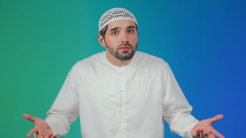 الإستفهام حول موضوع معين, الغموض وعدم الوضوح، بورتريه لرجل عربي خليجي اماراتي يرتدي الكندورة والقبعة البيضاء يرفع يديه نحو الأعلى بإيماءات عدم المعرفة, التساؤل والإستغراب والاستفسار عن أمر ما، خلفية ملونه