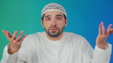 الغموض وعدم الوضوح، الإستفهام حول موضوع معين, بورتريه لرجل عربي خليجي اماراتي يرتدي الكندورة والقبعة البيضاء يرفع يديه نحو الأعلى بإيماءات عدم المعرفة, التساؤل والإستغراب والاستفسار عن أمر ما، خلفية ملونه