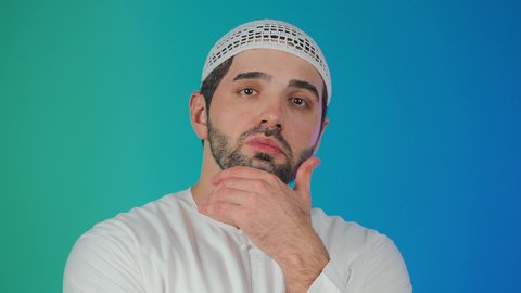 مفهوم الاستماع والتركيز، التطلع والتخطيط للمستقبل، حل المشكلات واتخاذ القرارات، بورتريه لرجل عربي خليجي اماراتي يرتدي الكندورة والقبعة البيضاء يضع يده على ذقنه بإيماءات التفكير وشرود الذهن،  خلفية ملونة