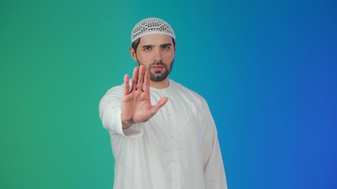 بورتريه لشاب عربي خليجي اماراتي يرتدي الكندورة والطاقية يمد كفه نحو الامام  بتعابير النهي عن فعل شيء ما, ايماءات الحزم والجدية, الصمت والتوقف عن الكلام, مفهوم الرفض والامتناع والانزعاج، خلفيه ملونة
