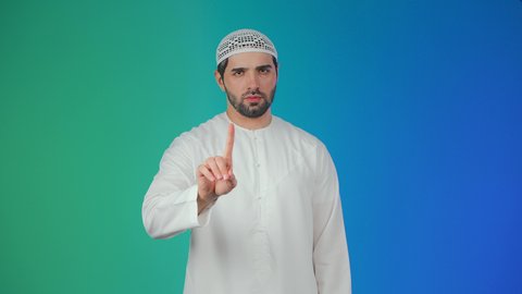 مفهوم الرفض والامتناع والانزعاج، بورتريه لشاب عربي خليجي اماراتي يرتدي الكندورة والطاقية يرفع اصبع السبابة بتعابير النهي عن فعل شيء ما, ايماءات الحزم والجدية, خلفيه ملونة