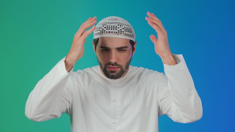 الأسف عل خسارة شيء ما ذو قيمة، خيبة الأمل والتعرض لخذلان وصدمة،الإحباط والحزن على ضياع الفرصة، بورتريه لرجل عربي خليجي  اماراتي يرتدي الكندورة والطاقية يضع يديه خلف رأسه بتعابير الحسرة والندم، خلفية ملونة