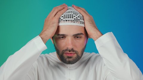 خيبة الأمل والتعرض لخذلان وصدمة، الأسف عل خسارة شيء ما ذو قيمة، الإحباط والحزن على ضياع الفرصة، بورتريه لرجل عربي خليجي  اماراتي يرتدي الكندورة والطاقية يضع يديه خلف رأسه بتعابير الحسرة والندم، خلفية ملونة