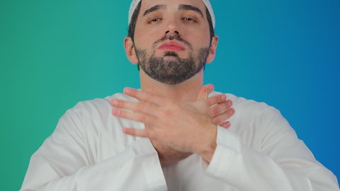 مفهوم الاهتمام بالصحة, الاصابة بنزلة برد والتهاب الحلق، الاحساس بألم البلعوم, الحاجة إلى العلاج والدواء,بورتريه لرجل عربي خليجي اماراتي يرتدي الكندورة والطاقية يضع يديه على حلقه ويشعر بالاختناق, خلفية ملونة