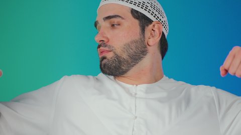 المواظبة على التمارين الرياضية، اتباع نظام غذائي صحي، الاهتمام باللياقة الجسدية،بناء الكتلة العضلية للجسم، مفهوم القوة والرجولة، بورتريه لرجل عربي خليجي  اماراتي يرتدي الكندورة والطاقية ينظر الى عضلاته بإيماءات السعادة، خلفية ملونة