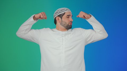 اتباع نظام غذائي صحي، الاهتمام باللياقة الجسدية، المواظبة على التمارين الرياضية، بناء الكتلة العضلية للجسم، مفهوم القوة والرجولة، بورتريه لرجل عربي خليجي  اماراتي يرتدي الكندورة والطاقية ينظر الى عضلاته بإيماءات السعادة، خلفية ملونة