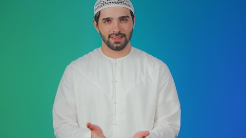 بورتريه لرجل عربي خليجي اماراتي يرتدي الكندورة والطاقية يرفع يده بايماءات حمل ورفع شيء ما، ايماءات السرور والسعاده، استخدام حاسة اللمس لرفع العناصر الهولوجراميه،خلفية ملونة