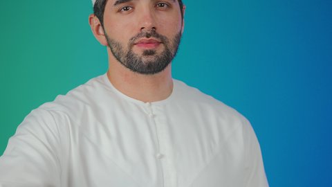 A portrait of an Emirati Arab man wearing a kandura and a headscarf, raising his left hand to greet, gestures indicating happiness, a concept of peace and welcome, various facial expressions and body language, colorful background.