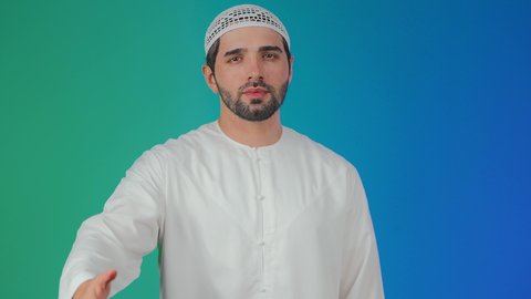 تعابير الوجه ولغة الجسد المختلفة, مفهوم السلام والترحيب, بورتريه لرجل عربي اماراتي خليجي يرتدي الكندورة والطاقية يرفع اليد اليسري لإلقاء التحية, ايماءات تدل على السعادة, خلفية ملونة