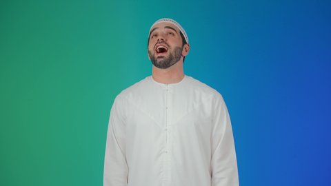 بورتريه مقرب لرجل عربي اماراتي خليجي يرتدي الكندورة و الطاقيه ينظر الى الكاميرا بتعابير الضحك الهستيري, الشعور بالفرح والسعادة، ايماءات البهجة والسرور الشديد،خلفية ملونه