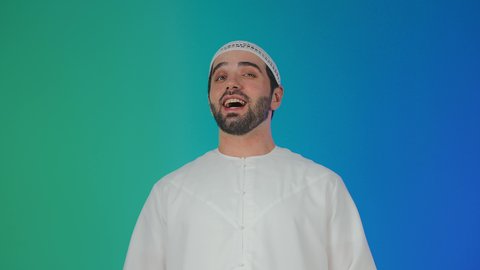 ايماءات البهجة والسرور الشديد، الشعور بالفرح والسعادة، بورتريه مقرب لرجل عربي اماراتي خليجي يرتدي الكندورة و الطاقيه ينظر الى الكاميرا بتعابير الضحك الهستيري, خلفية ملونه