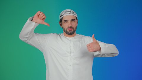 Confusion and hesitation regarding a matter, a portrait of an Arab Gulf Emirati man wearing a kandura and a headscarf, raising his thumb up and down with gestures of disagreement and agreement, dislike and like, the concept of rejection and acceptance, colorful background.