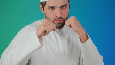احتراف رياضة الملاكمة، إغلاق اليدين والاستعداد للهجوم والمواجهة، محاولة الدفاع عن النفس، مفهوم القوة والرجولة، بورتريه لرجل عربي خليجي اماراتي يرتدي الكندورة والطاقية ينظر للكاميرا بإيماءات الجدية والغضب،  خلفية ملونة