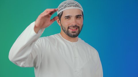 تعابير الوجه ولغة الجسد المختلفة, مفهوم السلام والترحيب, بورتريه لرجل عربي اماراتي خليجي يرتدي الكندورة والطاقية يرفع اليد اليمني لإلقاء التحية, ايماءات السرور والسعادة, خلفية ملونة