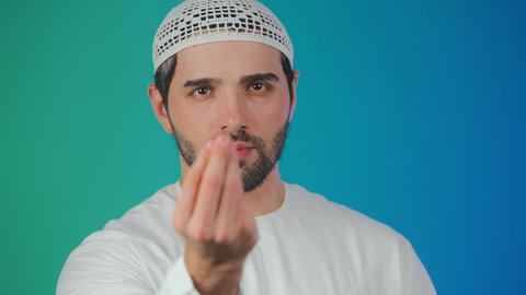 بورتريه لرجل عربي خليجي اماراتي يرتدي الكندورة والطاقية ينظر الى الكاميرا يرفع يده نحو الأعلى بإيماءات طلب الإنتظار, مفهوم الصبر والتريث و التأني, التهديد و التوعد لشيء ما،خلفية ملونة