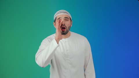 Conversations and social communication, calling out loudly, placing the hand next to the mouth to amplify the sounds, a portrait of a young Emirati Arab man wearing a kandura and a headscarf looking at the camera with gestures calling someone, shouting and speaking in a loud tone to be heard well, colorful background.