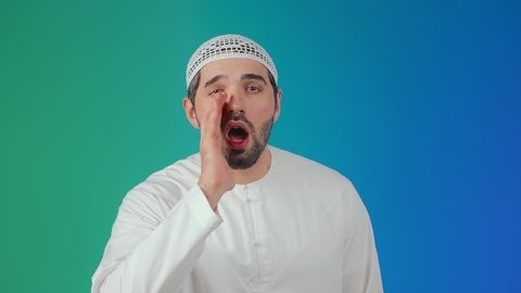 وضع اليد بجانب الفم لزيادة حدة الأصوات،النداء بصوت مرتفع,  بورتريه لشاب عربي خليجي اماراتي يرتدي الكندورة والطاقية ينظر إلى الكاميرا بإيماءات المناداة لشخص ما، الصراخ والتكلم بنبرة عالية للسماع بشكل جيد، محادثات وتواصل اجتماعي، خلفية ملونة