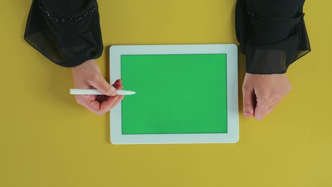 The use of modern tools in correction processes, a vertical overhead shot of the hand of an Arab Gulf Saudi woman wearing a black abaya using a tablet with a blank green screen and drawing a check mark on the tablet, the use of technology and modern techniques, chroma.