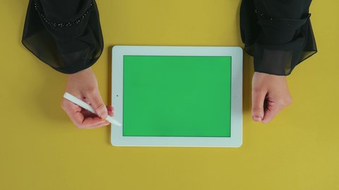 استعمال الوسائل المتطورة في التصحيح, تصوير علوي عامودي ليد امرأة عربية خليجية سعودية ترتدي العباءة السوداء تستخدم تابلت بشاشة خضراء فارغة و تقوم برسم اشارة الصح على الجهاز اللوحي, استخدام التكنولوجيا و التقنيات الحديثة، كروما