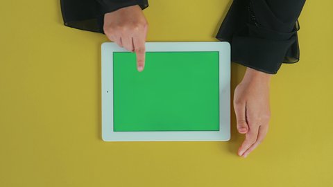 تصفح مواقع و وسائل التواصل الاجتماعي، استعمال جهاز تقني حديث لتصفح الصور والفيديوهات بسهولة، استخدام التكنولوجيا في الترفيه، عرض شاشة كروما خضراء فارغة, تصوير علوي عامودي مقرب ليد امرأة عربية خليجية سعودية تستخدم التابلت
