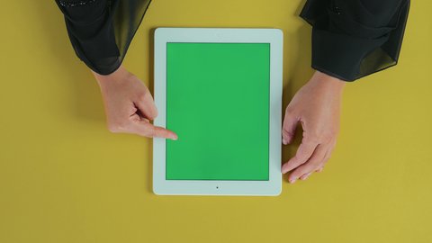 التنقل بين البرامج, استخدام التكنولوجيا في الترفيه، عرض شاشة كروما خضراء فارغة, تصوير علوي عامودي ليد امرأة عربية خليجية سعودية ترتدي العباءة السوداء تستخدم التابلت, تصفح مواقع و وسائل التواصل الاجتماعي