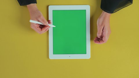 استخدام التكنولوجيا و التقنيات الحديثة، استعمال الوسائل المتطورة في التصحيح, تصوير علوي عامودي ليد امرأة عربية خليجية سعودية  تستخدم تابلت بشاشة خضراء فارغة و تقوم برسم اشارة الصح على الجهاز اللوحي، كروما