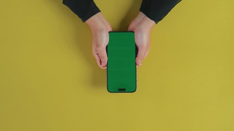 Watching movies and series using a mobile phone, entertainment and enjoying leisure time, the concept of entertainment with modern technology and technology, an overhead close-up shot of the hand of a Saudi Gulf Arab woman using the phone to watch a video, displaying a blank green chroma screen.