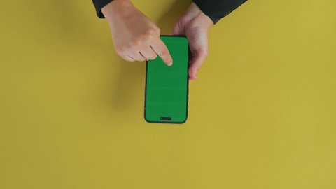 التحكم بالشاشة بإيماءات النقر، عرض شاشة خضراء كروما فارغة، مفهوم الترفيه بالتقنية والتكنولوجيا الحديثة، متابعة الافلام والمسلسلات عبر الجوال، التسلية والاستمتاع بالاستراحة، تصوير علوي عامودي مقرب ليد امرأة عربية خليجية سعودية تستخدم الهاتف المحمول