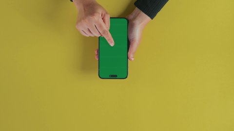 الضغط على شاشة الجهاز، عرض شاشة خضراء كروما فارغة، مفهوم الترفيه بالتقنية والتكنولوجيا الحديثة، متابعة الافلام والمسلسلات عبر الجوال، التسلية والاستمتاع بالاستراحة، تصوير علوي عامودي مقرب ليد امرأة عربية خليجية سعودية تستخدم الهاتف المحمول