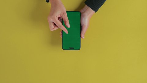 A blank green chroma screen is displayed, the concept of entertainment with modern technology and technology, watching movies and series via mobile, fun and enjoying the break, an overhead close-up shot of the hand of a Saudi Gulf Arab woman using the phone to watch something.