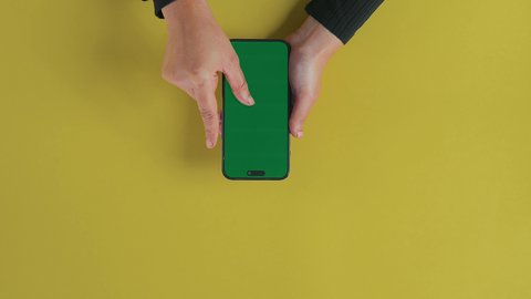 A blank green chroma screen is displayed, the concept of entertainment with modern technology and technology, watching movies and series via mobile, fun and enjoying the break, an overhead close-up shot of the hand of a Saudi Gulf Arab woman using the phone to watch something.