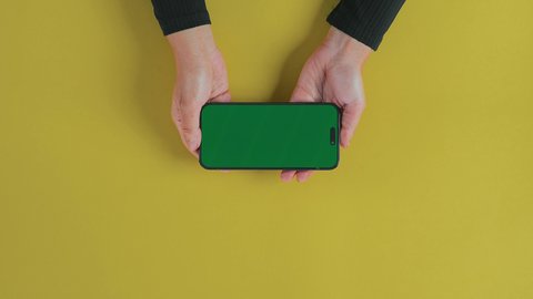 التسلية والاستمتاع بالاستراحة، مفهوم الترفيه بالتقنية والتكنولوجيا الحديثة، تصوير علوي عامودي ليد امرأة عربية خليجية سعودية ترتدي العباءة السوداء و تستخدم الهاتف لمشاهدة فيديو, متابعة الافلام والمسلسلات عبر الجوال, عرض شاشة خضراء كروما فارغة