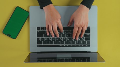 الكتابة على لوحة المفاتيح، إرسال بريد الكتروني عبر الحاسوب, استخدام التقنيات الحديثة و المتطورة في العمل, عقد الاجتماعات عبر الانترنت، تصوير علوي عامودي ليد امرأة عربية خليجية سعودية ترتدي العباءة السوداء تستخدم اللابتوب و بجانبها هاتف محمول بشاشة خضراء فارغة, كروما