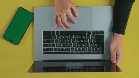 خاصية تكبير الصور في الحاسوب المحمول, استخدام التقنيات الحديثة والمتطور ة في العمل, عقد الاجتماعات عبر الانترنت، تصوير علوي عامودي ليد امرأة عربية خليجية سعودية ترتدي العباءة السوداء تستخدم اللابتوب و بجانبها هاتف محمول بشاشة خضراء فارغة, كروما