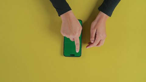 Supervising remote work, tapping gestures on the phone, displaying an empty green chroma screen, the concept of entertainment with modern technology and technology, watching movies and series via mobile, an overhead close-up shot of the hand of an Arab Gulf Saudi woman wearing a black abaya and using a mobile phone.