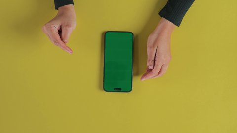 ايماءات النقر على الشاشة، عرض شاشة خضراء كروما فارغة، مفهوم الترفيه بالتقنية والتكنولوجيا الحديثة، متابعة الافلام والمسلسلات عبر الجوال، التسلية والاستمتاع بالاستراحة، تصوير علوي عامودي مقرب ليد امرأة عربية خليجية سعودية تستخدم الهاتف المحمول