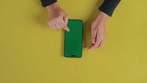 متابعة آخر أخبار السوشال ميديا, عرض شاشة خضراء فارغة على الأجهزة التقنية، استخدام التكنولوجيا الحديثة لإنجاز المهام عن بُعد، لقطة عامودية من الأعلى ليد امرأة عربية خليجية سعودية ترتدي العباءة السوداء  و تستخدم هاتفًا محمولًا, كروما