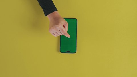 Chatting and conversations with friends, following the latest social media news, displaying a blank green screen on technical devices, using modern technology to accomplish tasks remotely, a vertical shot from above of the hand of a Saudi Gulf Arab woman wearing a black abaya and using a mobile phone, chroma.