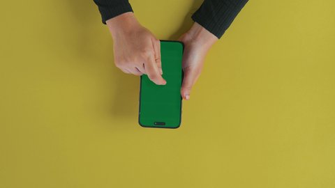 Exchanging conversations with family and friends, following the latest social media news, displaying a blank green screen on technical devices, using modern technology to accomplish tasks remotely, a vertical shot from above of the hand of a Saudi Gulf Arab woman wearing a black abaya and using a mobile phone, chroma.