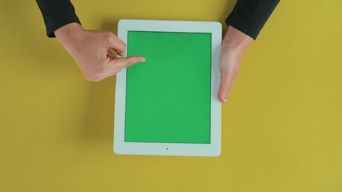 Using touch functionality, applications and programs for tablets, using technology and modern techniques, the concept of project management and completing tasks remotely, an overhead vertical shot of the hand of an Arab Gulf Saudi woman wearing a black abaya using a tablet with a blank green screen, chroma.