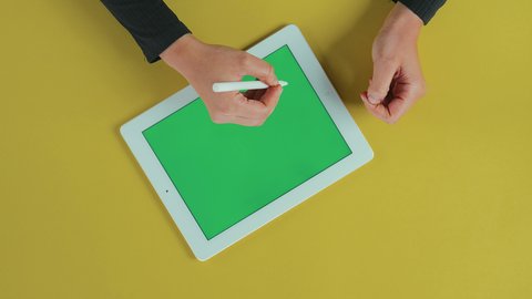 إحتراف وظائف التكنولوجيا و استعمال القلم الخاص بالجهاز اللوحي، رسم الصور و التصاميم, استخدام التقنيات الحديثة، مفهوم إدارة المشاريع وانجاز المهام عن بعد، تصوير علوي عامودي ليد امرأة عربية خليجية سعودية ترتدي العباءة السوداء تستخدم تابلت بشاشة خضراء فارغة, كروما