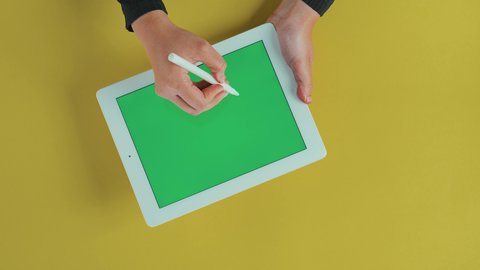 Professionalism in technology jobs and the use of the tablet's stylus, the concept of project management and completing tasks remotely, using modern technologies, an overhead close-up shot of the hand of a Saudi Arabian Gulf Arab woman using a tablet with a blank green screen, chroma.