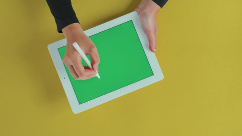 Using the tablet's stylus, mastering technology functions, the concept of project management and completing tasks remotely, using modern technologies, an overhead close-up shot of the hand of a Saudi Gulf Arab woman using a tablet with a blank green screen, chroma.