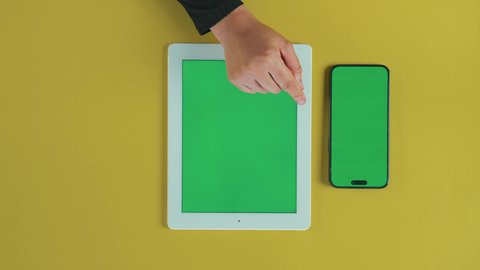 النقر على شاشة الجهاز اللوحي, التطور التقني والتكنولوجي في مختلف المجالات, متابعة مواقع التواصل الاجتماعي، تصوير علوي عامودي ليد امرأة عربية خليجية سعودية ترتدي العباءة السوداء تستخدم التابلت و هاتف محمول بشاشة خضراء فارغة, كروما