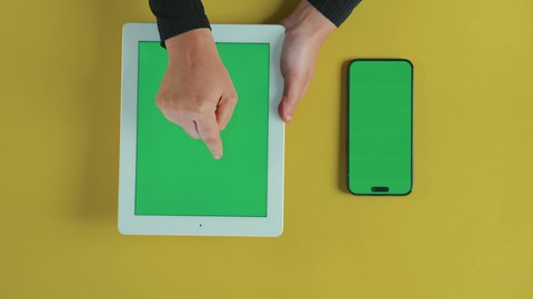 Accomplishing tasks professionally, monitoring social media, applications and programs for tablets, using technology and modern techniques, an overhead vertical shot of the hand of an Arab Gulf Saudi woman wearing a black abaya using a tablet, with a mobile phone beside her with a blank green screen, chroma.