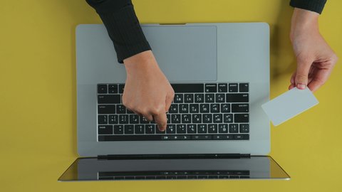 الكتابة عبر النقر على الكيبورد، دمج العمل مع التقنية والتكنولوجيا، إدارة شؤون الأعمال وتنظيمها عبر الأجهزة الحديثة، الشراء والدفع عن بعد، تصوير علوي عامودي ليدين رجل عربي سعودي خليجي يرتدي الثوب التقليدي و يقوم باستخدام بطاقة الإئتمان و اللابتوب