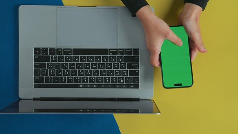 تسهيل نقل البيانات, متابعة مواقع التواصل الاجتماعي، عقد الاجتماعات عبر الانترنت، تصوير علوي عامودي ليد امرأة عربية خليجية سعودية ترتدي العباءة السوداء تستخدم اللابتوب و تحمل هاتف محمول بشاشة خضراء فارغة, كروما